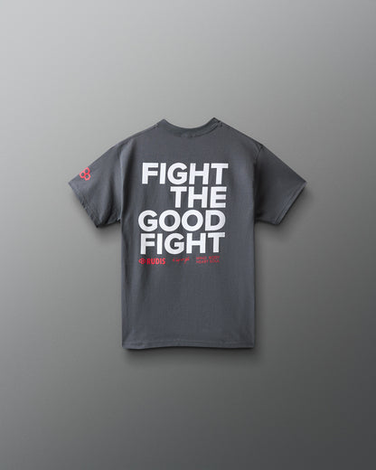 A dark gray short-sleeve t-shirt with bold white text reading 'FIGHT THE GOOD FIGHT' on the back, plus small red text and a small red logo on the left sleeve, shown against a smooth gray background.