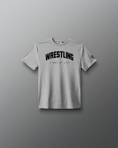 A light gray heather crewneck t-shirt with 'WRESTLING' printed in bold black letters across the chest, with 'A WAY OF LIFE' underneath, displayed on a dark gray gradient background.