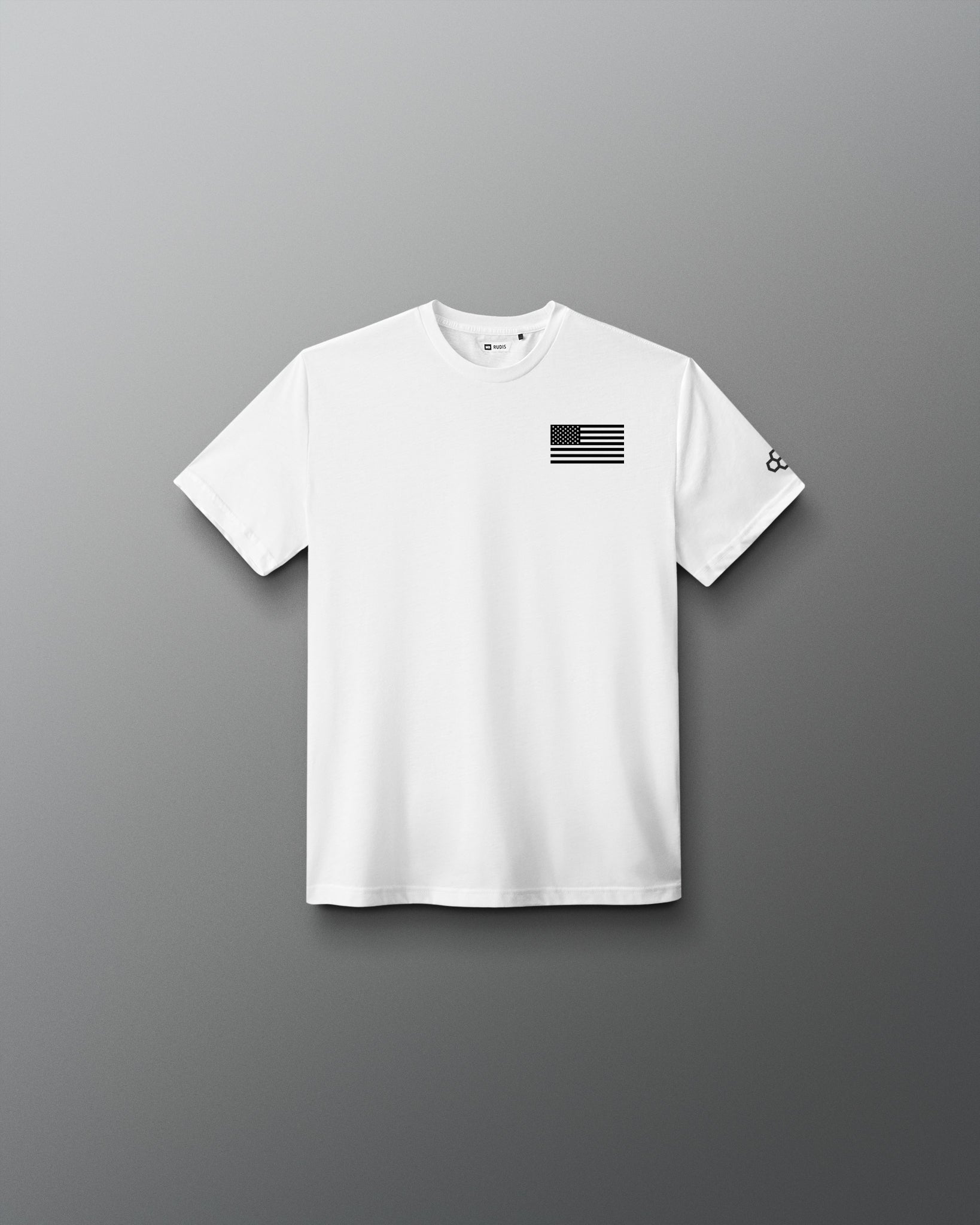Youth white RUDIS Core Flag Elite Super Soft T-Shirt shown from the front, featuring a black American flag graphic on the left chest and contrasting RUDIS mark on the sleeve.