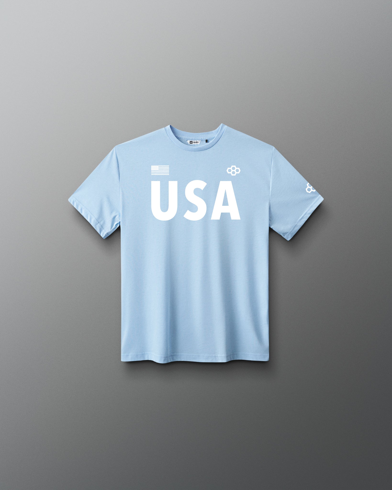 Front view of RUDIS USA Youth Elite Super Soft T-Shirt in light blue, featuring white USA lettering, an American flag graphic, RUDIS Hex logos, and short sleeves.