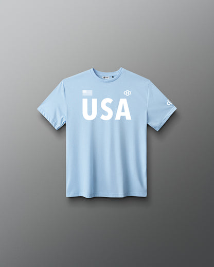 Front view of RUDIS USA Youth Elite Super Soft T-Shirt in light blue, featuring white USA lettering, an American flag graphic, RUDIS Hex logos, and short sleeves.
