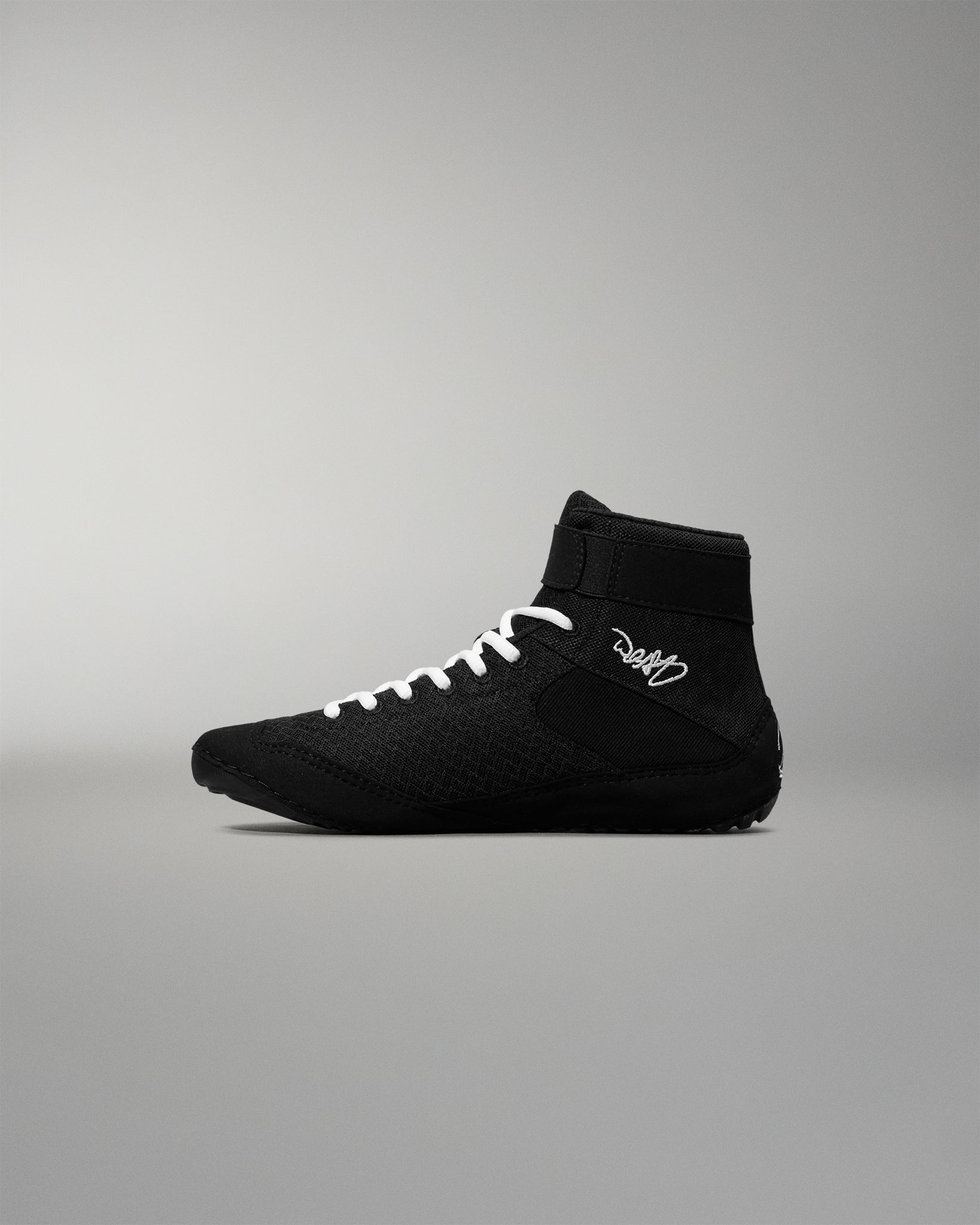 Black wrestling shoe with white laces on a gray background