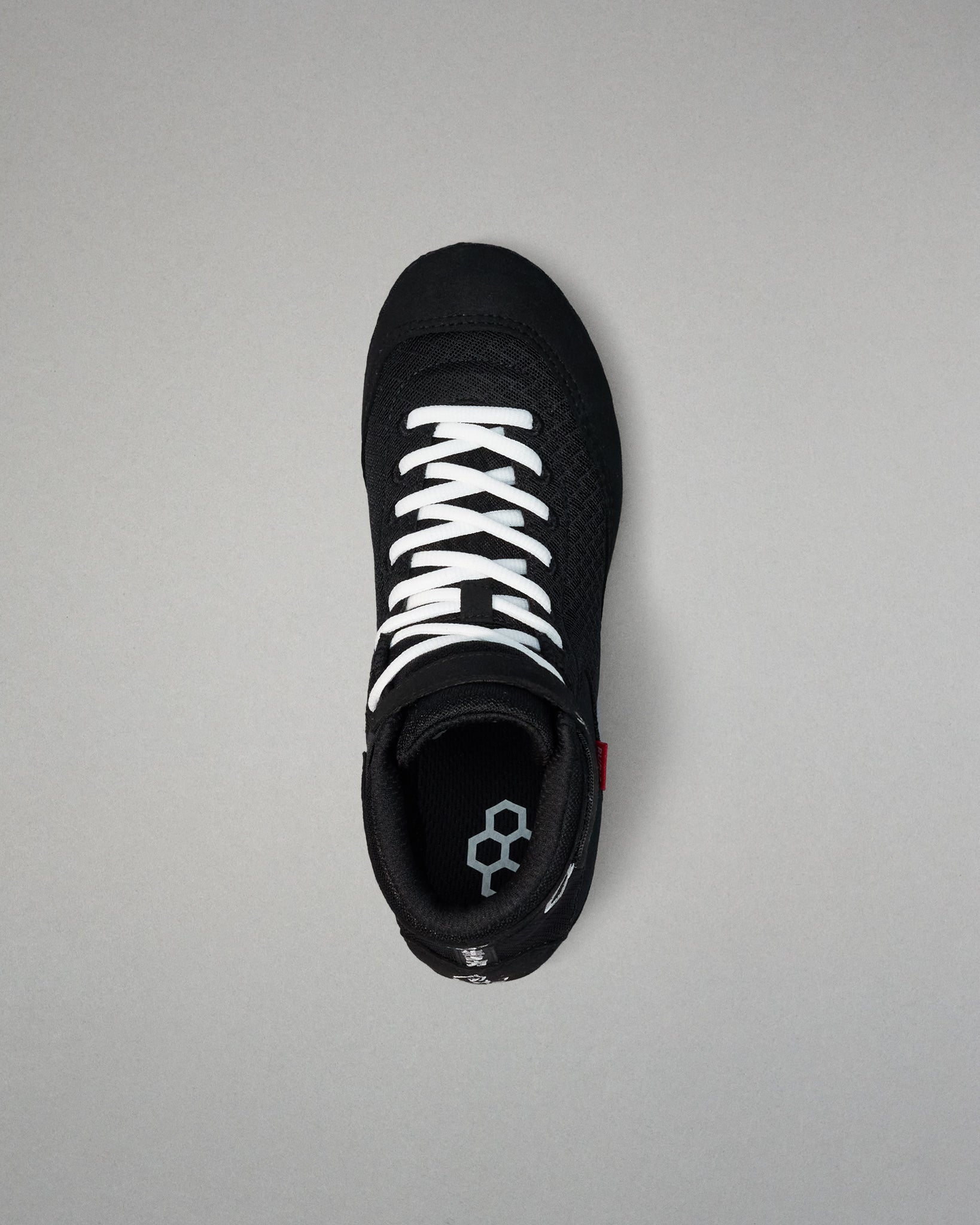 Black wrestling shoe with white laces on a gray background