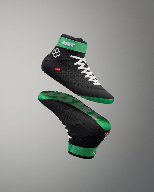 Black and green wrestling shoes with white laces on a gray background