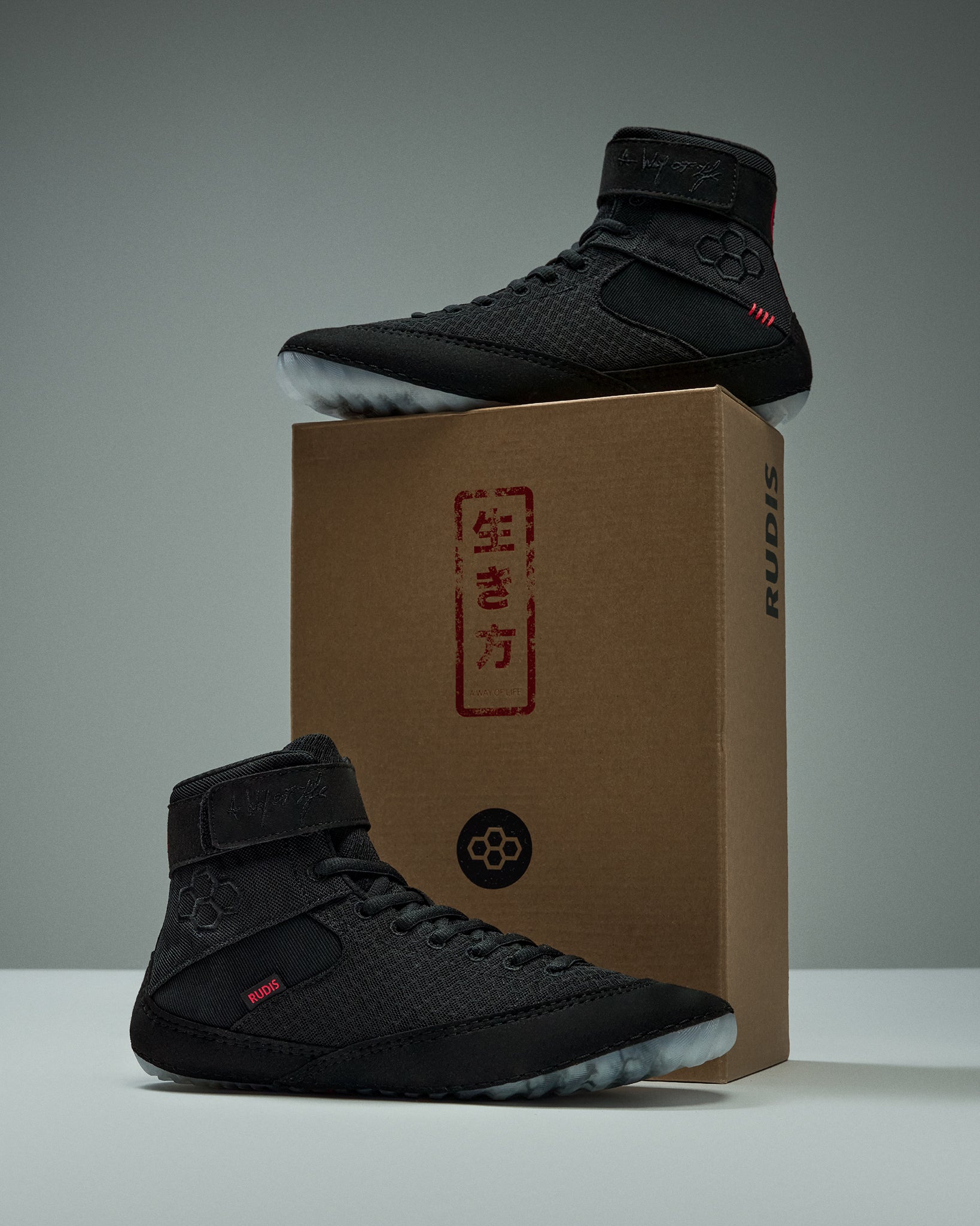 RUDIS Samurai Speed Youth Wrestling Shoes in Wabi-Sabi black displayed on and beside a RUDIS shoebox featuring red Japanese-inspired lettering and branding.