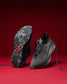 Black athletic shoe with red sole detail on a red background