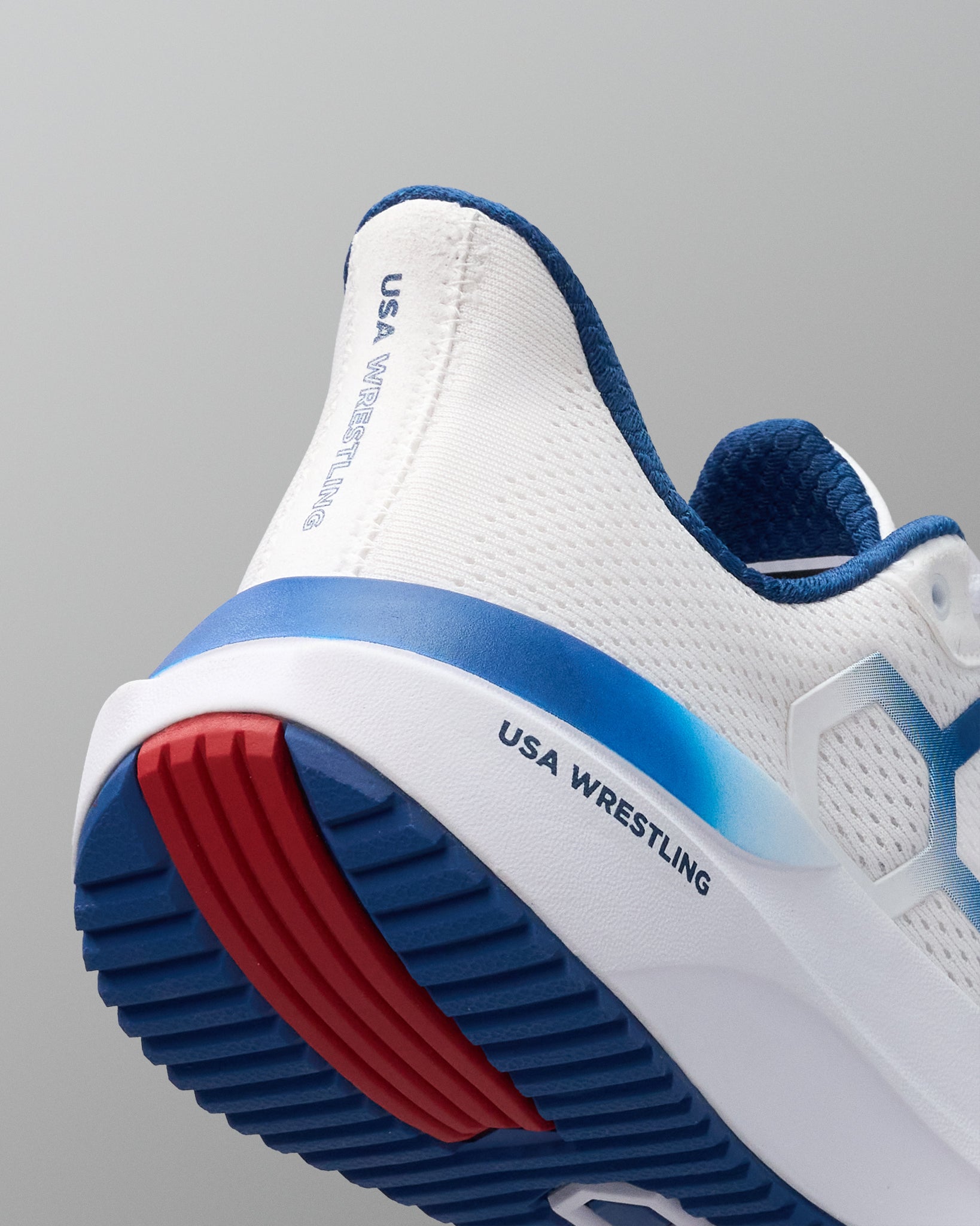 White athletic shoe with blue and red sole on a gray background