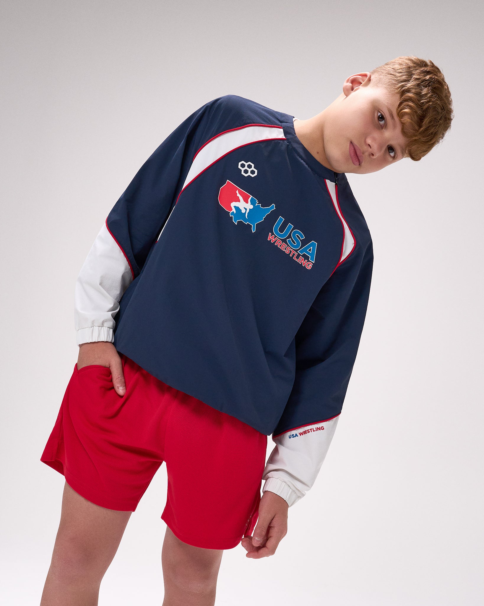 Person wearing a navy sweatshirt with USA Wrestling logo and red shorts on a white background