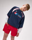Person wearing a navy sweatshirt with USA Wrestling logo and red shorts on a white background