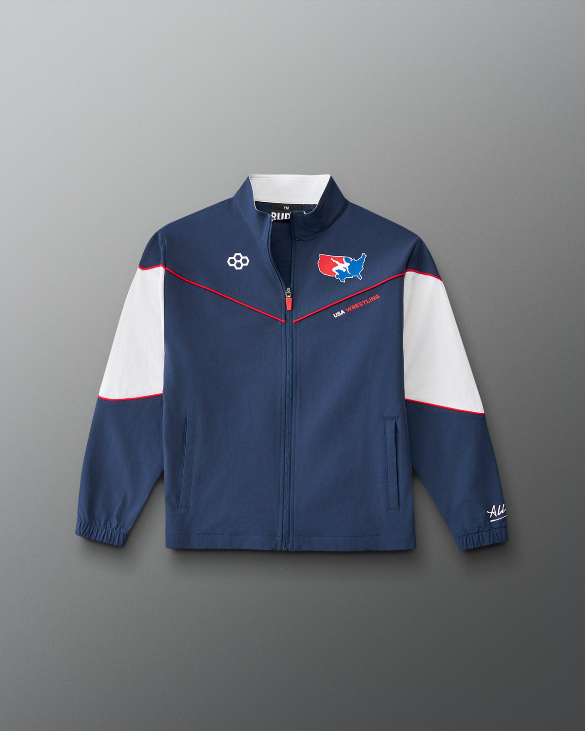 A navy blue zip-up track jacket with white shoulder panels and thin red piping details, featuring team-style graphics on the chest, photographed against a neutral gray background.