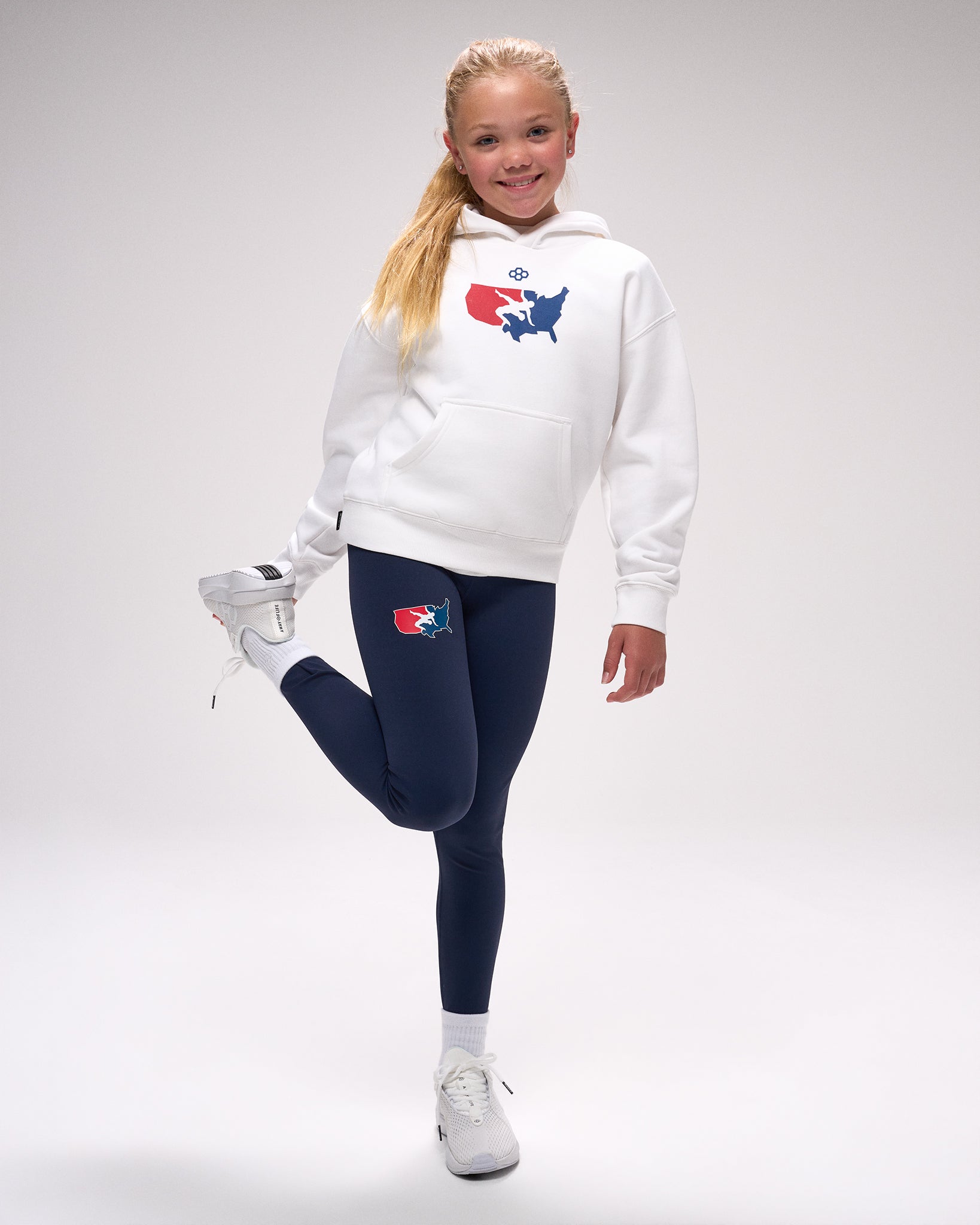 Person wearing a white hoodie and navy leggings with 'USA Wrestling' logos, posing against a gray background