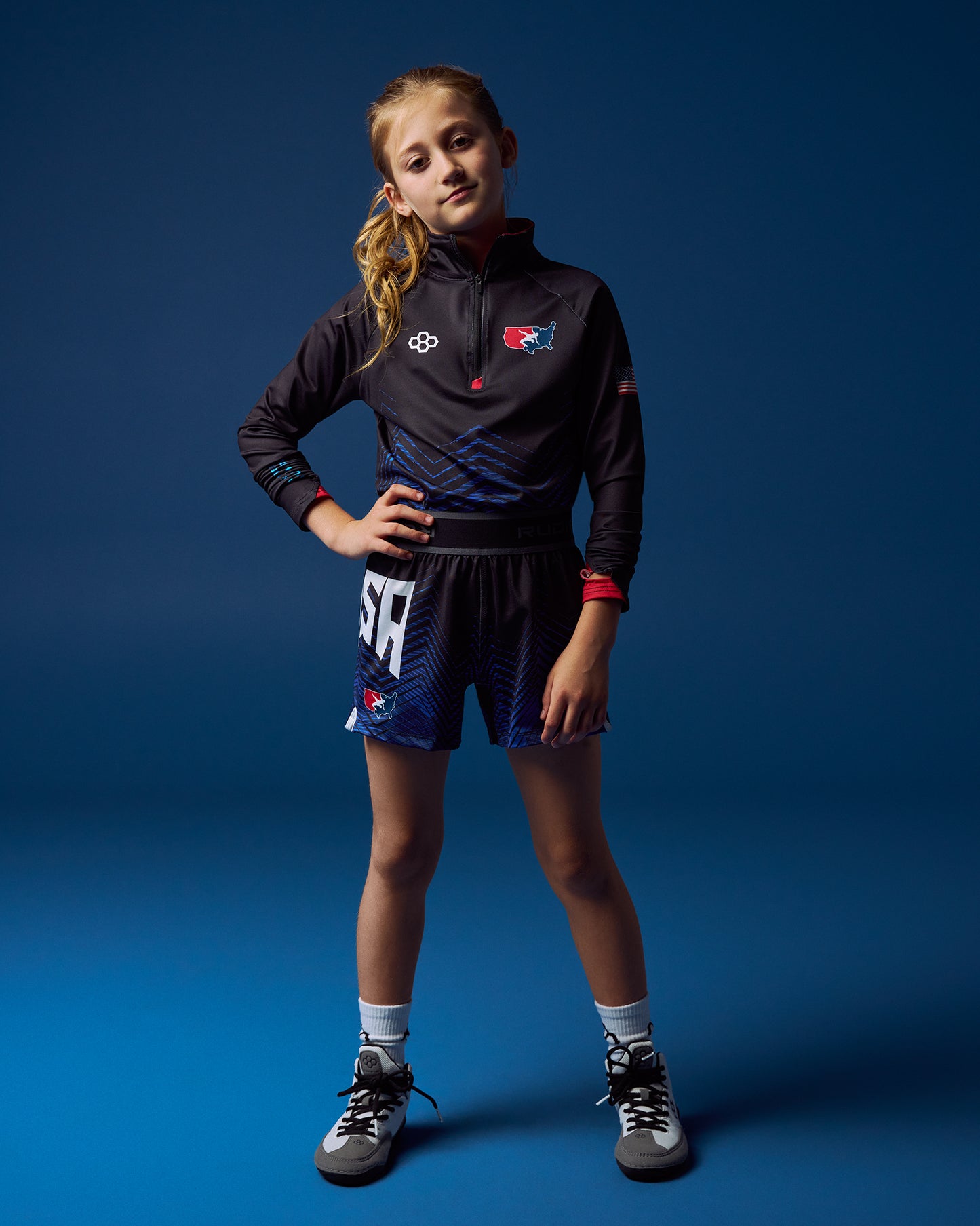 Young girl in RUDIS USA Wrestling sports attire posing against a blue background