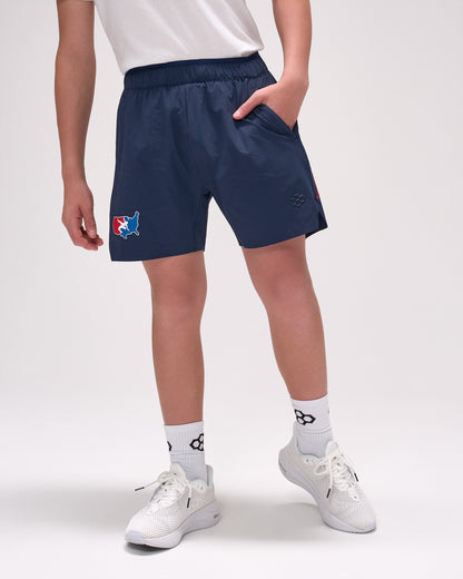 Person wearing navy shorts with a logo, white shirt, and white sneakers on a light gray background