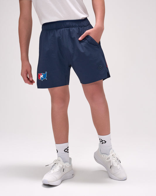 Person wearing navy shorts with a logo, white shirt, and white sneakers on a light gray background