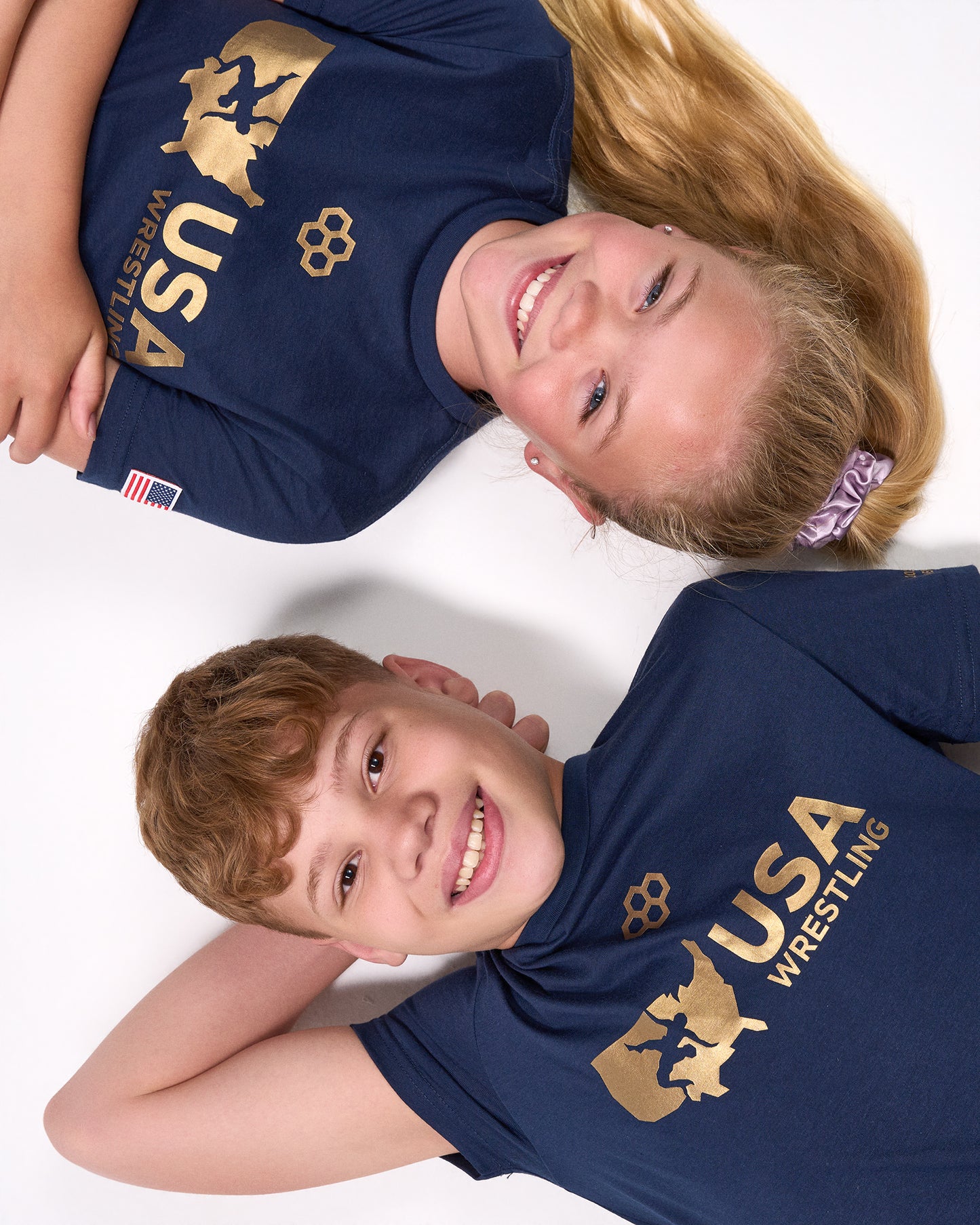 Two children wearing navy blue USA Wrestling t-shirts on a white background