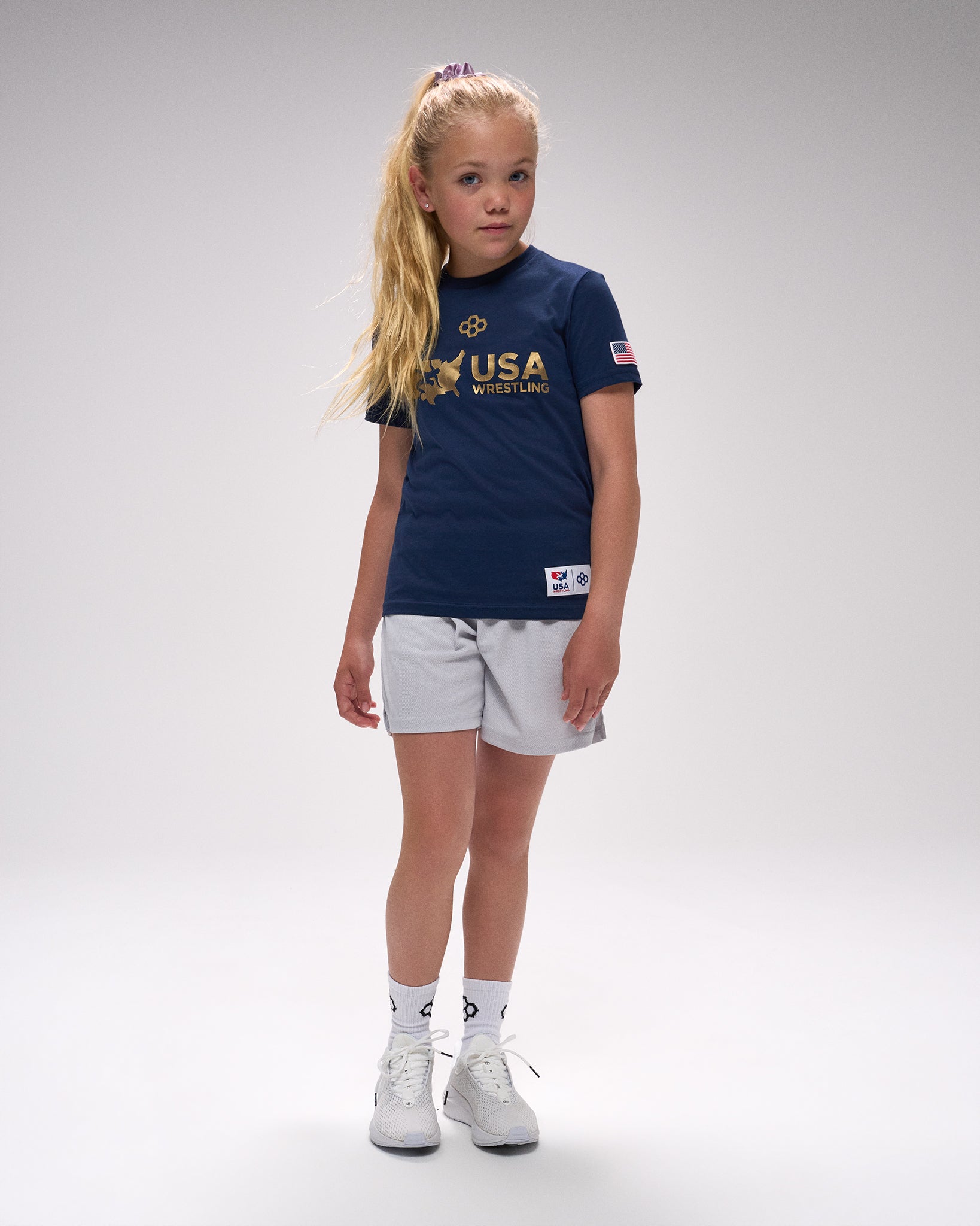Young girl wearing a USA Wrestling t-shirt and shorts on a gray background