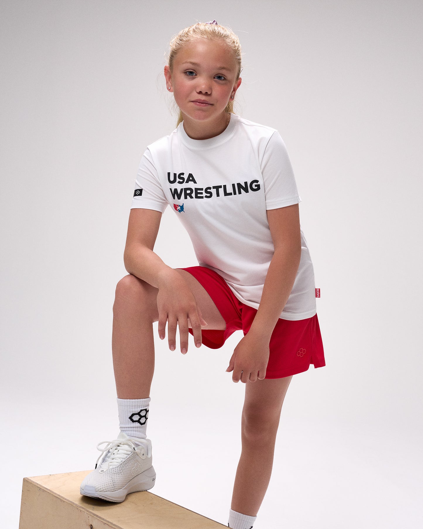 Child wearing a USA Wrestling t-shirt and red shorts on a white background