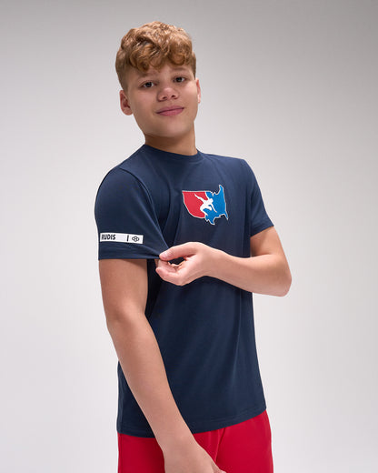 Young boy wearing a navy blue t-shirt with a logo on a gray background