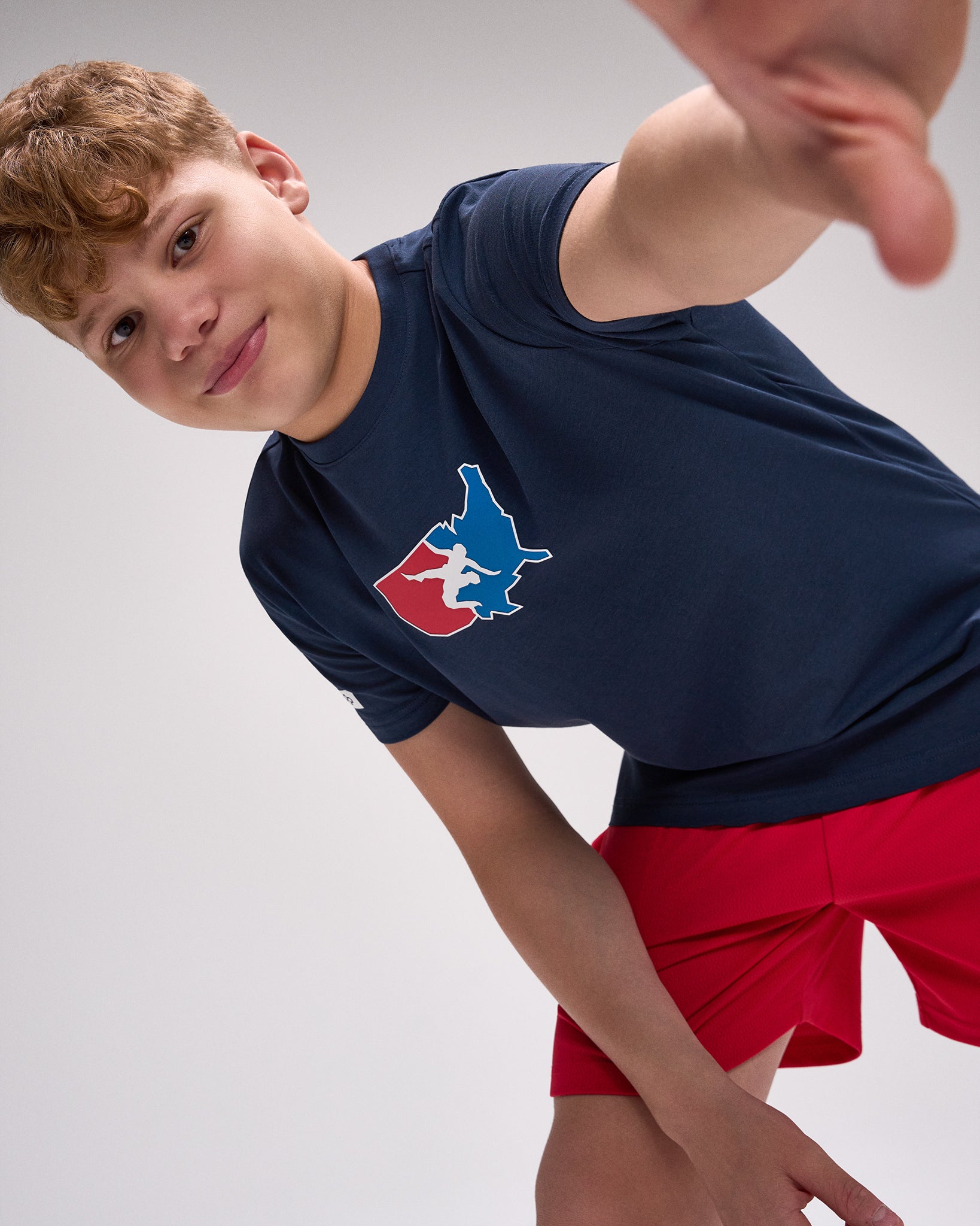 Person wearing a navy blue t-shirt with a logo and red shorts on a light gray background