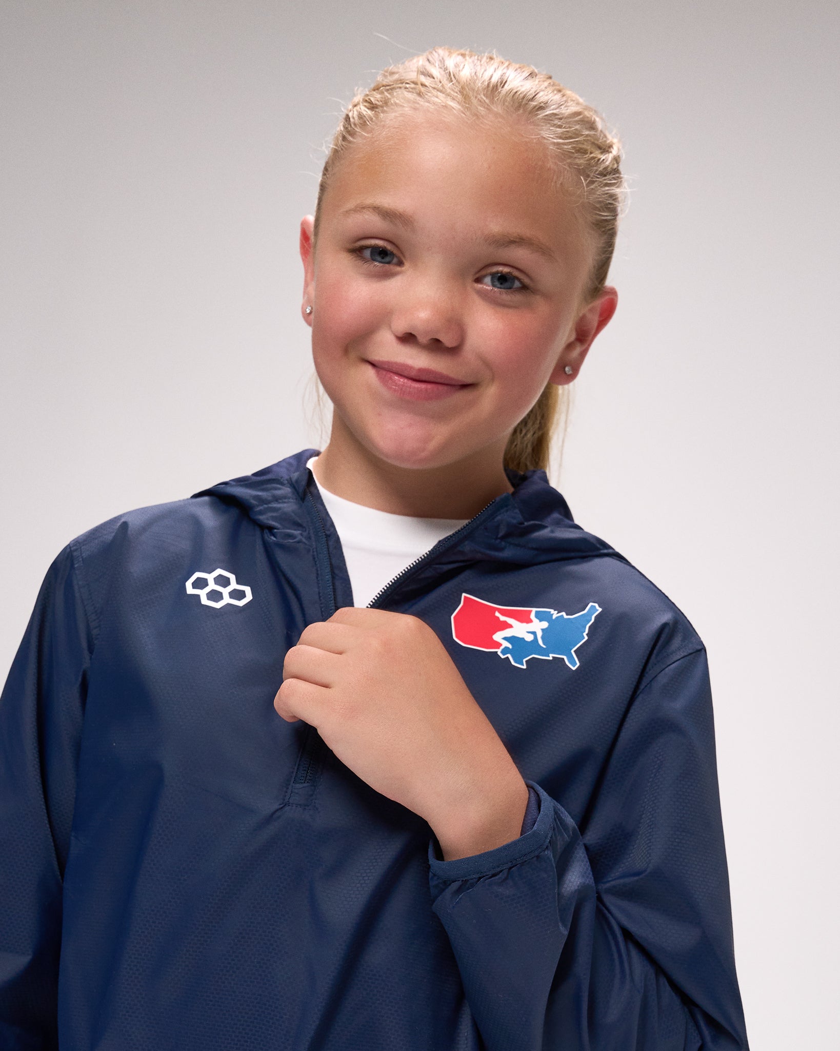 Young girl wearing a blue jacket with a logo on a gray background