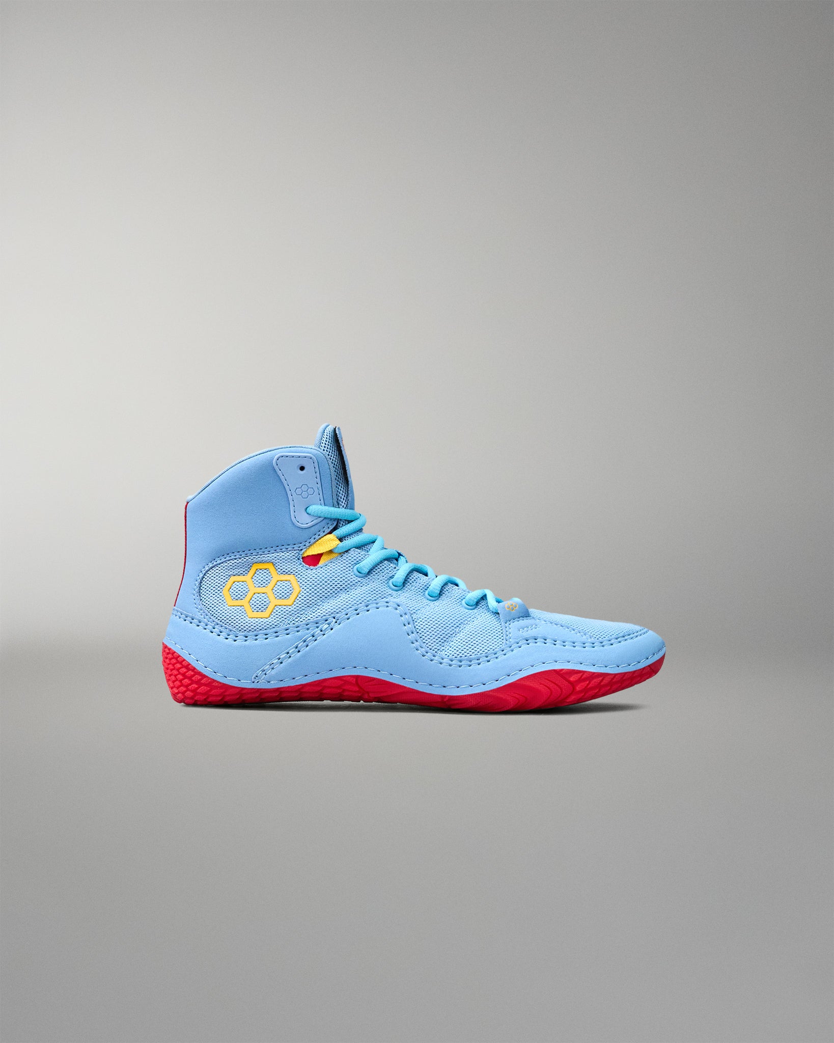 Side profile of RUDIS JB1 Superman wrestling shoe showing light blue mesh upper, yellow RUDIS logo and red traction outsole.