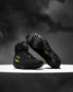 A pair of black high-top wrestling shoes with yellow Batman-themed accents, including a Batman logo on the side and a yellow circular emblem on the sole, displayed on a white platform against a dark smoky background.