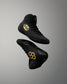 Two black high-top wrestling shoes floating against a gray gradient background. One shoe displays a yellow Batman logo on the side, and the other shows a yellow honeycomb pattern on the sole.