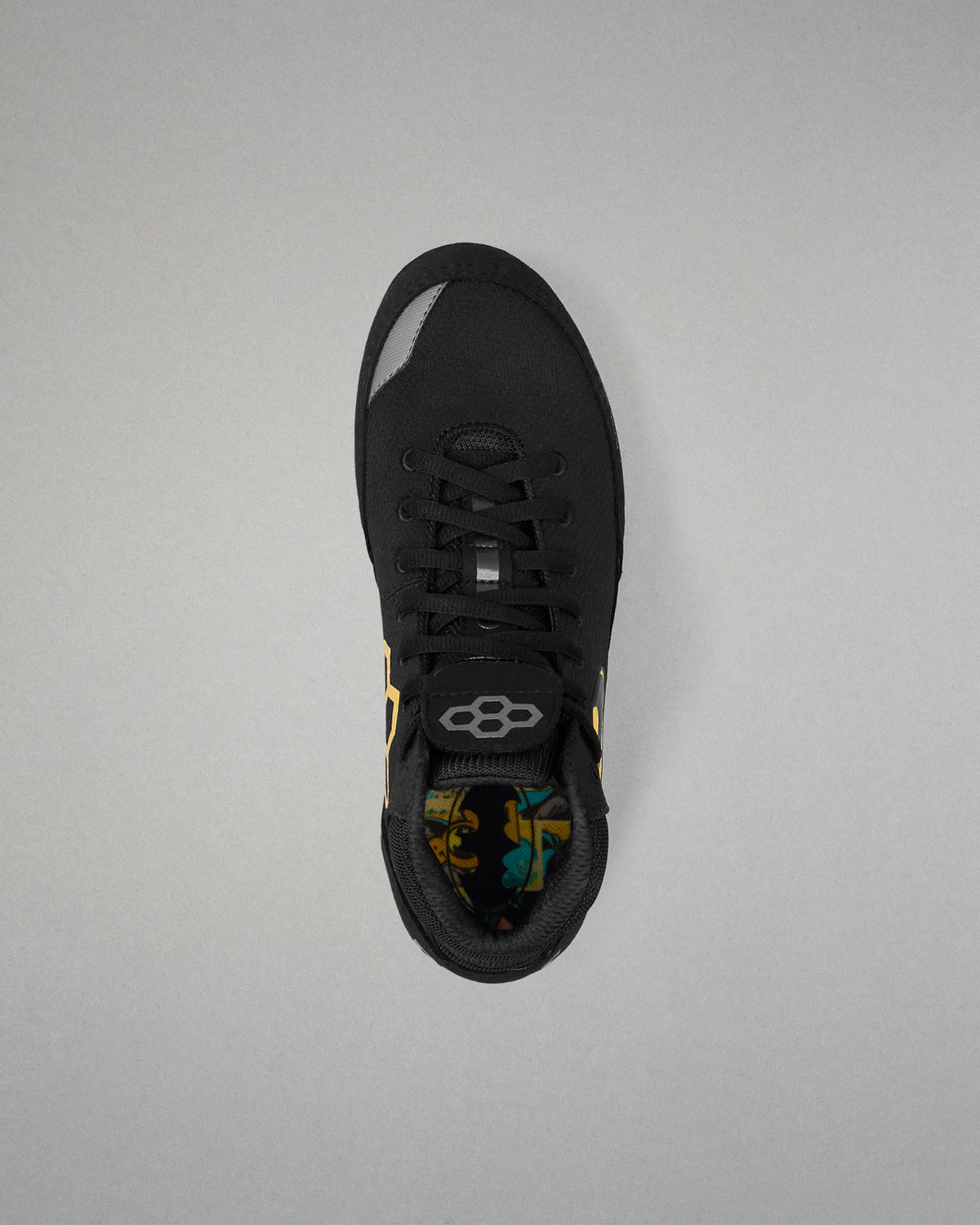 A black athletic wrestling shoe shown from a top-down view against a neutral gray background. The shoe features a black mesh upper, black laces, a black heel counter, and a small yellow accent on the side.