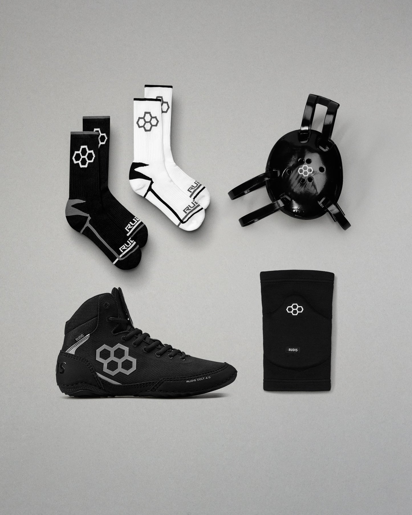 Collection of black and white wrestling gear including shoes, socks, and kneepads on a gray background.