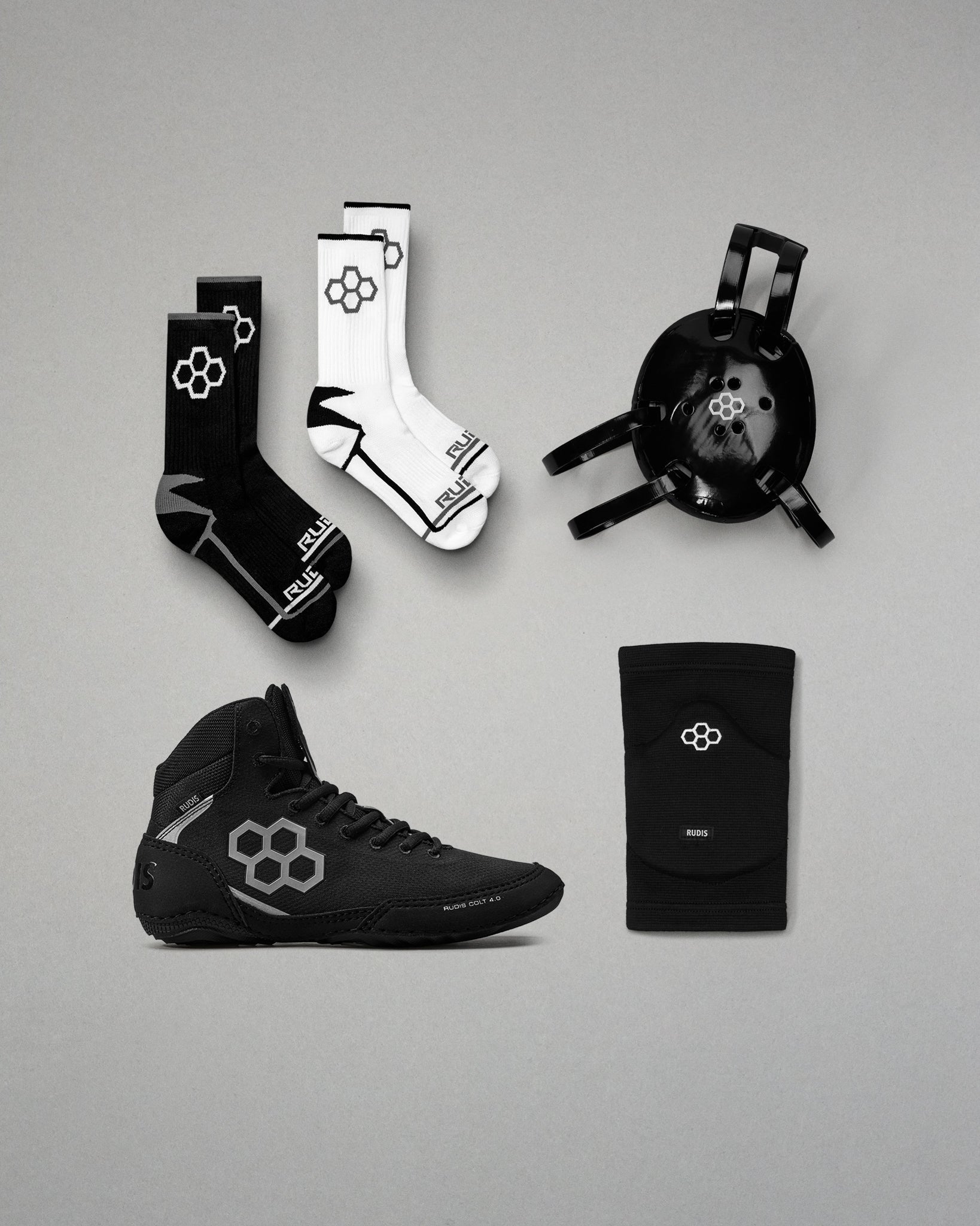Collection of black and white wrestling gear including shoes, socks, and kneepads on a gray background.